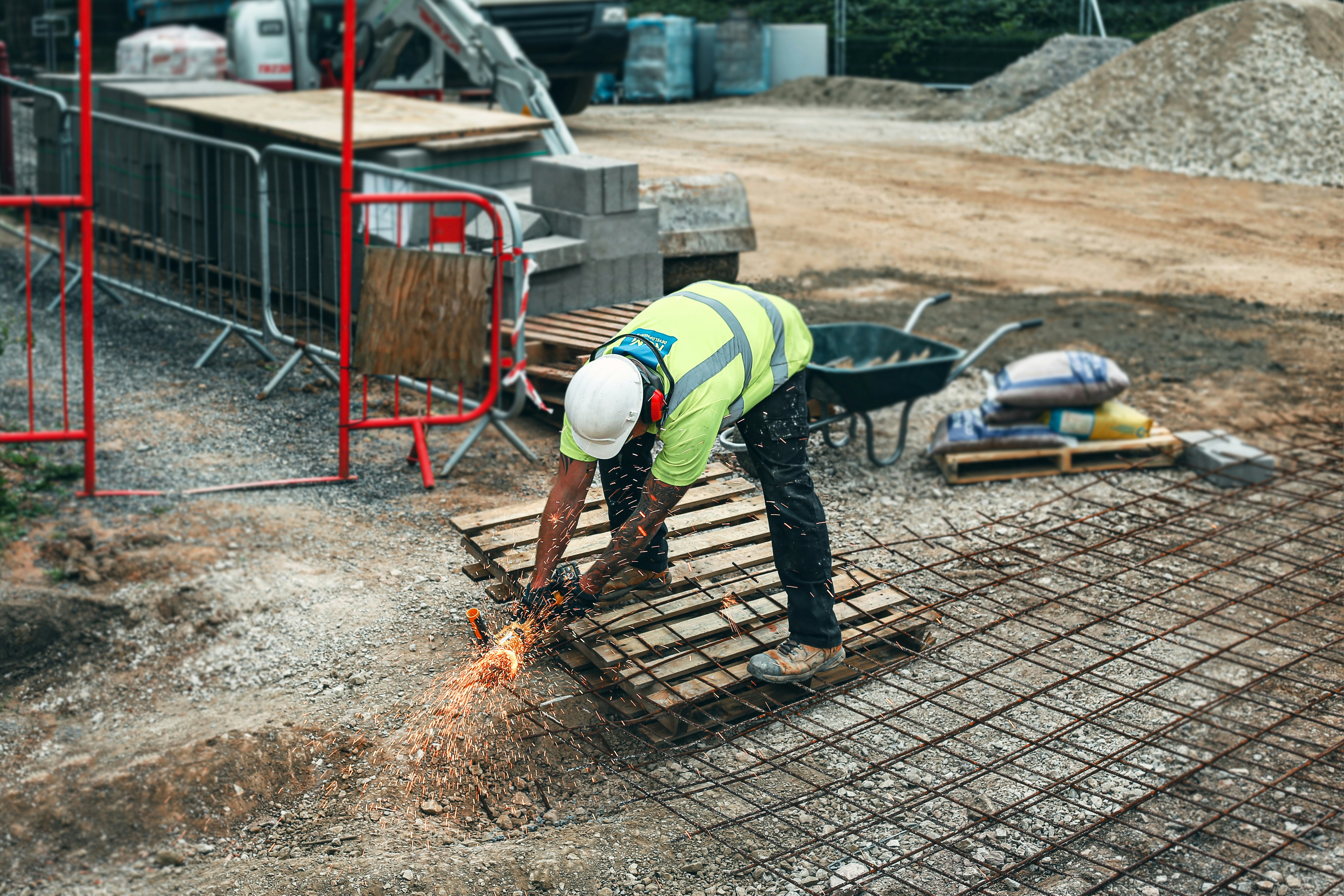 Civil worker bent over cutting steel mesh with an angle grinder on a construction site — work that takes a toll on backs, knees, shoulders, and hands